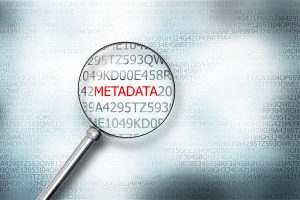 Looking at the word metadata on digital computer screen with a magnifying glass.